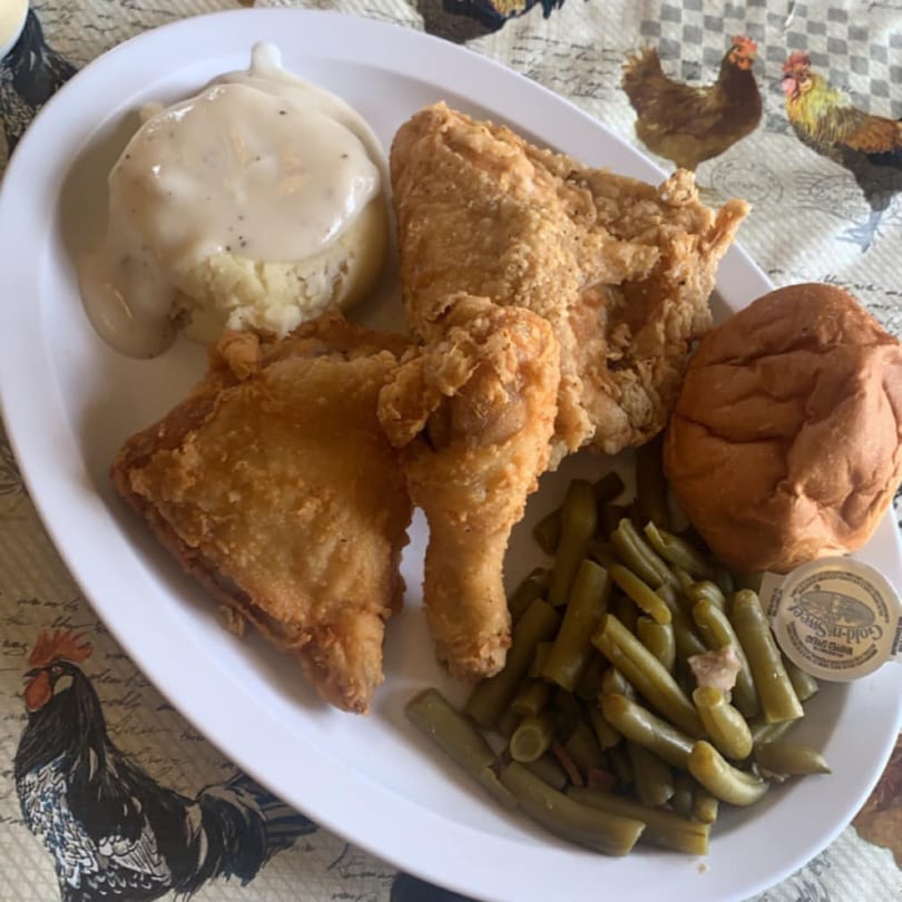 Fried chicken, mashed potatoes with gravy, green beans, and a roll on a white plate.