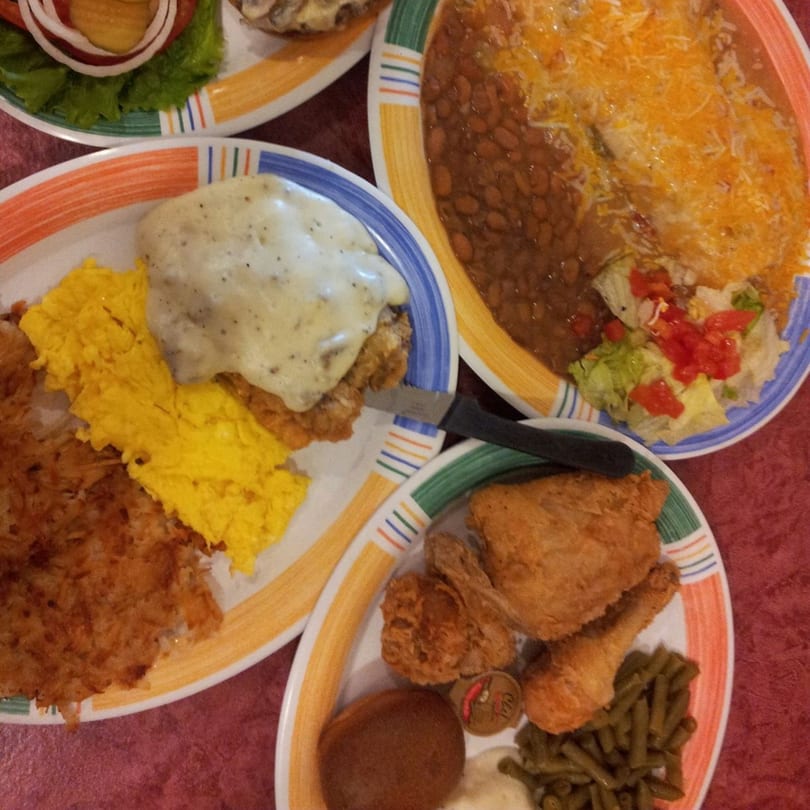 Overhead view of multiple plates of breakfast food, including chicken fried steak, eggs, hash browns, and beans.