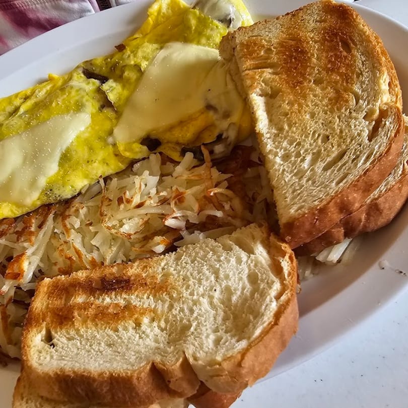 A breakfast plate from Hen House Cafe with cheesy scrambled eggs, crispy hash browns, and toasted bread.