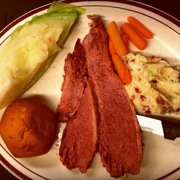 Corned beef with cabbage, mashed potatoes, carrots, and a dinner roll on a plate.
